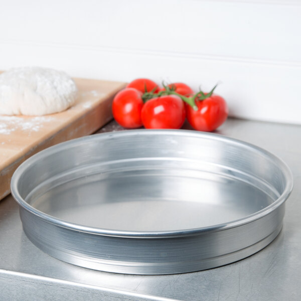 An American Metalcraft heavy weight aluminum round cake pan on a counter with dough and tomatoes on it.