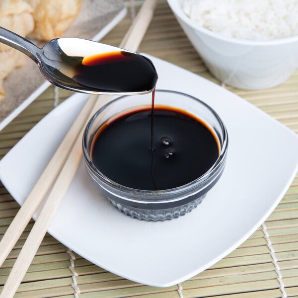 A spoon pouring Kikkoman Traditionally Brewed Soy Sauce into a bowl of rice.