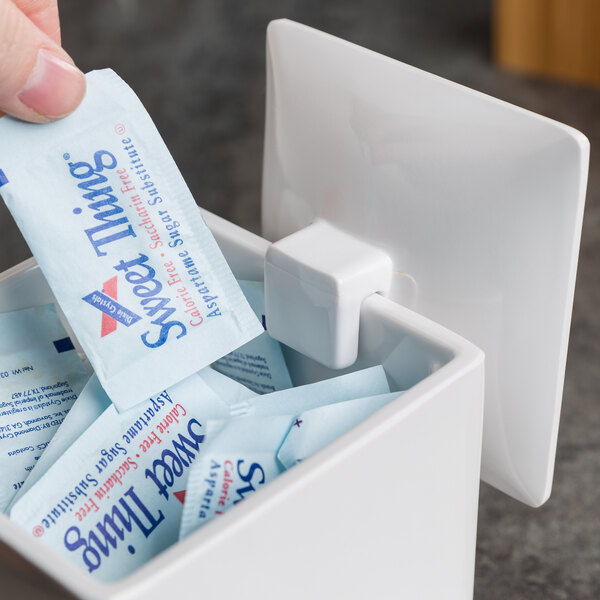A hand putting sugar packets in a white Cal-Mil container lid.
