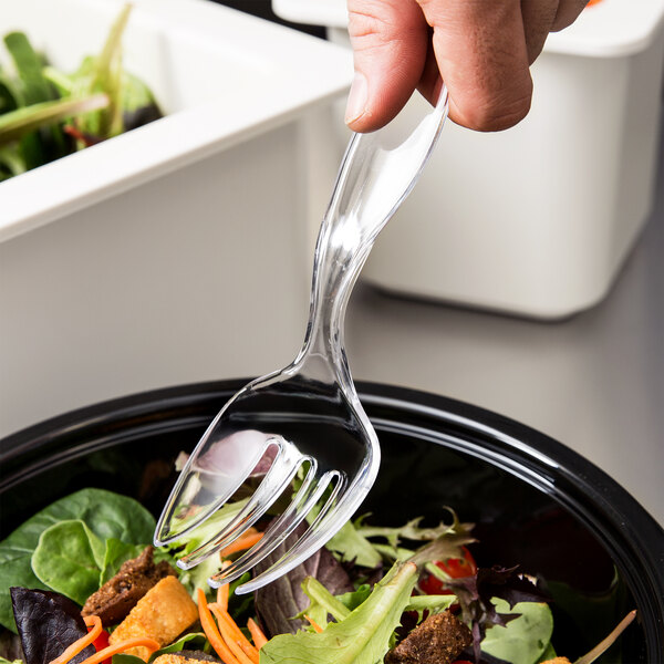 A hand holds a Fineline clear plastic serving fork over a salad.
