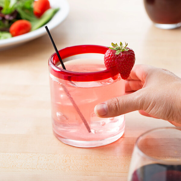 A hand holding a Libbey Aruba rocks glass with a pink drink and a strawberry on the rim.
