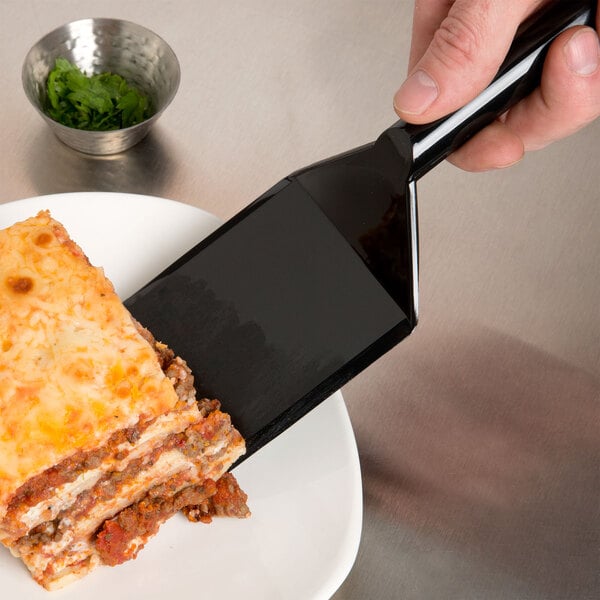 A hand holding a Fineline black disposable spatula over a plate of lasagna.