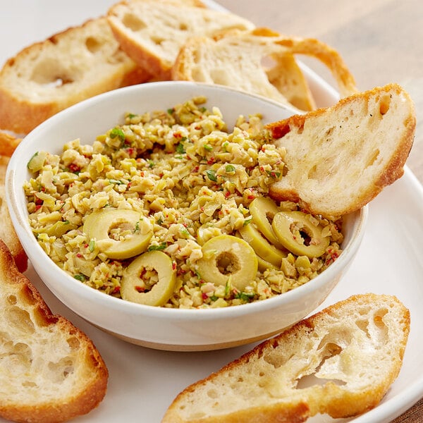 A bowl of Pitted Queen Olives on a table with bread.