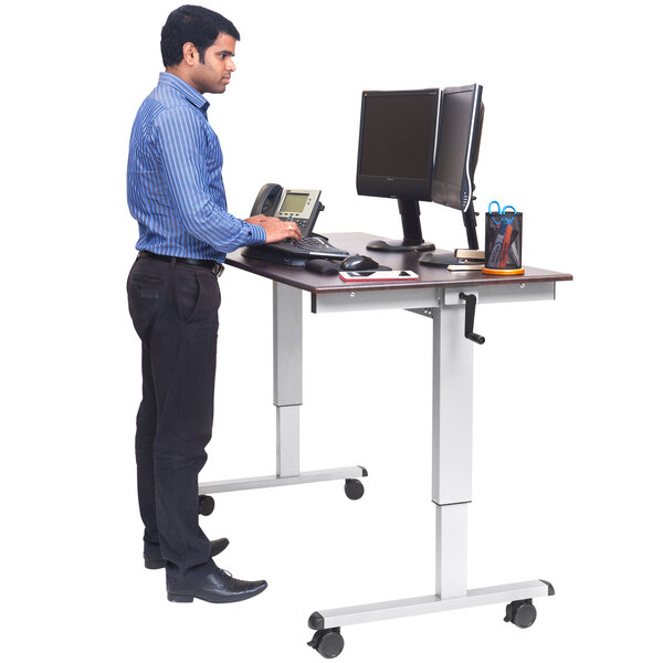 A man using a Luxor stand up desk with a laptop.