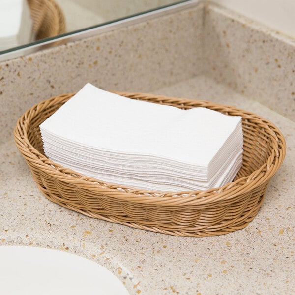 A basket of Lavex white paper guest towels on a bathroom counter.