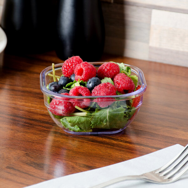 A Dinex clear square bowl with fruit and lettuce on a table.