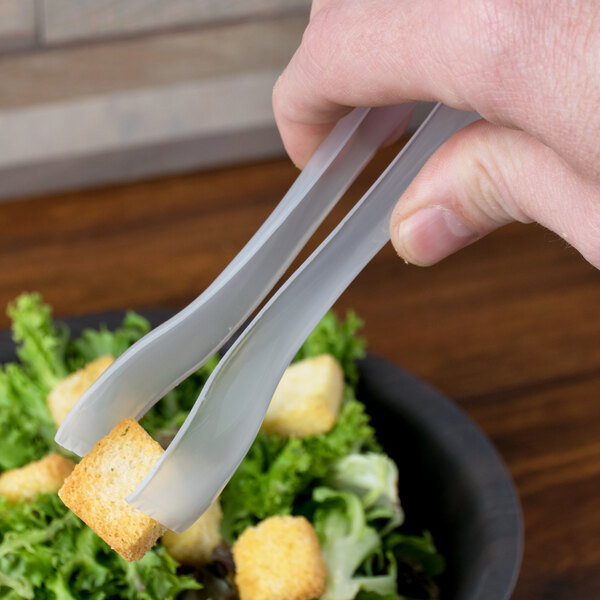 A person using Visions clear plastic tongs to serve salad.