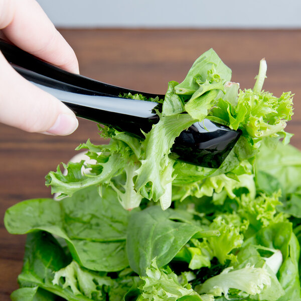 A person using black Visions tongs to pick up lettuce.
