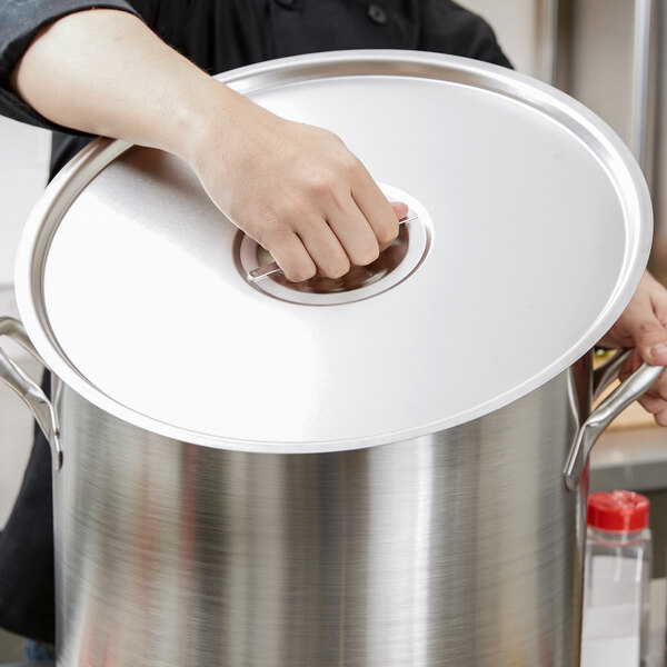 A hand holding a Vollrath stainless steel pot lid.