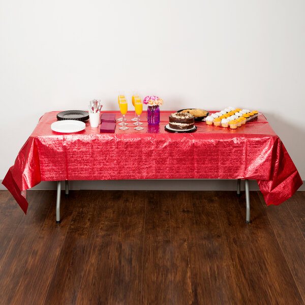 A table with a red Creative Converting plastic table cover and food on it.