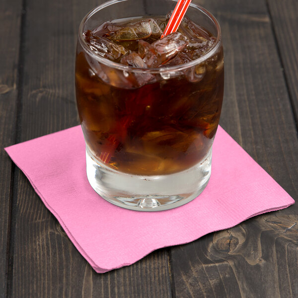 A glass of iced tea with a straw on a pink napkin.