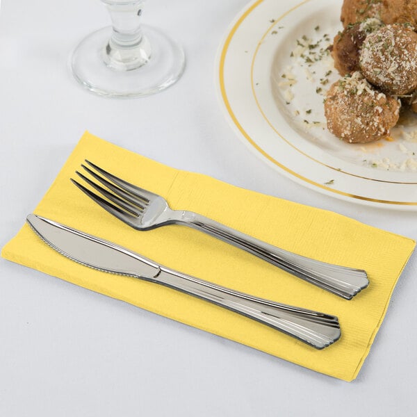 A fork and knife on a yellow Creative Converting dinner napkin.