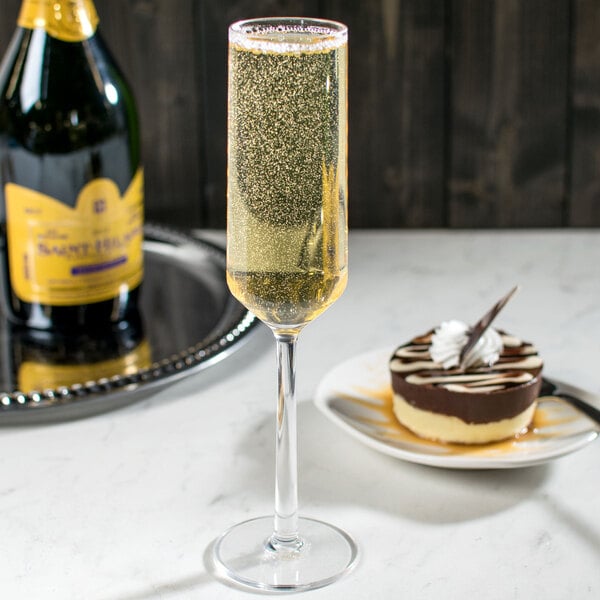 A customizable Tritan plastic champagne flute filled with yellow liquid next to a plate of chocolate cake on a table.