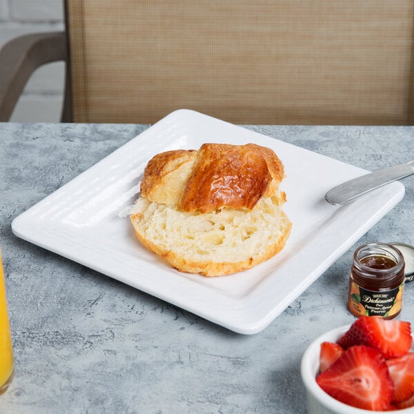 A white Elite Global Solutions square melamine plate with a croissant and strawberries on it.