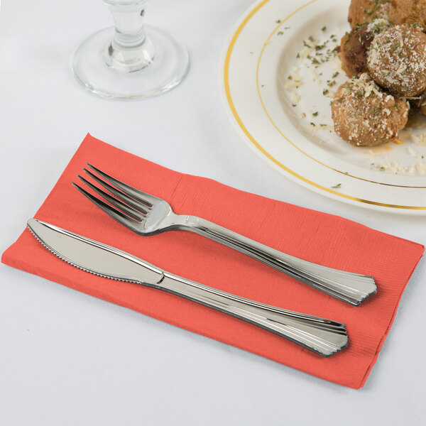 A fork and knife on a coral orange Creative Converting paper dinner napkin.