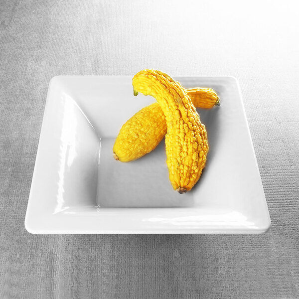 A white square Elite Global Solutions melamine bowl with yellow squashes inside.