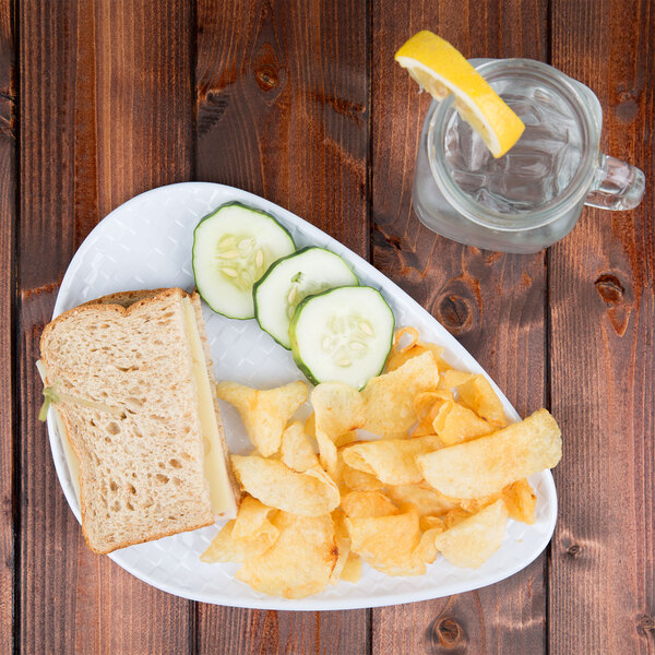 A sandwich on a white Coralline triangle melamine plate with chips and a glass of water.
