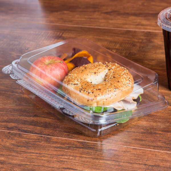 A plastic container with a bagel sandwich and fruit in it.