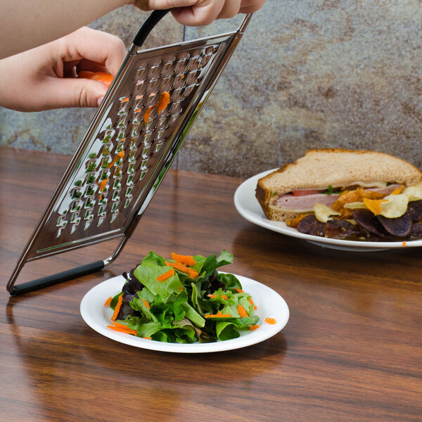 A person grating a plate of salad using a Tablecraft flat grater.