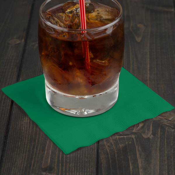 A glass of ice tea with a straw sitting on a green Creative Converting beverage napkin.