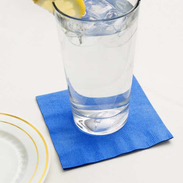 A glass of water on a blue Creative Converting beverage napkin with a slice of lemon on top.
