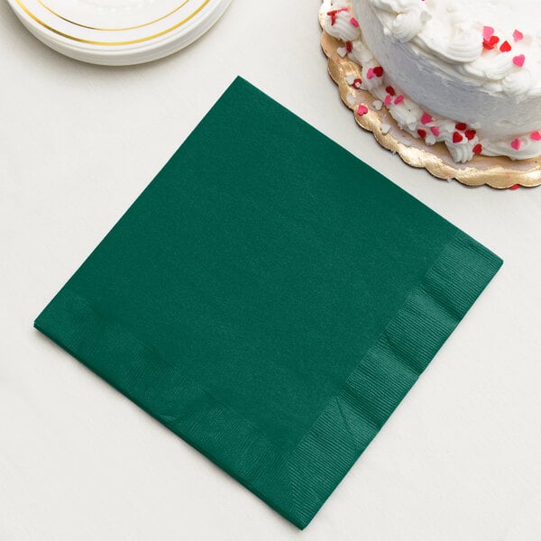 A stack of hunter green paper dinner napkins with a slice of white cake on top.