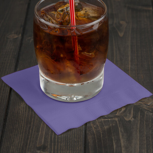 A glass of ice tea with ice and a straw sitting on a purple Creative Converting beverage napkin.