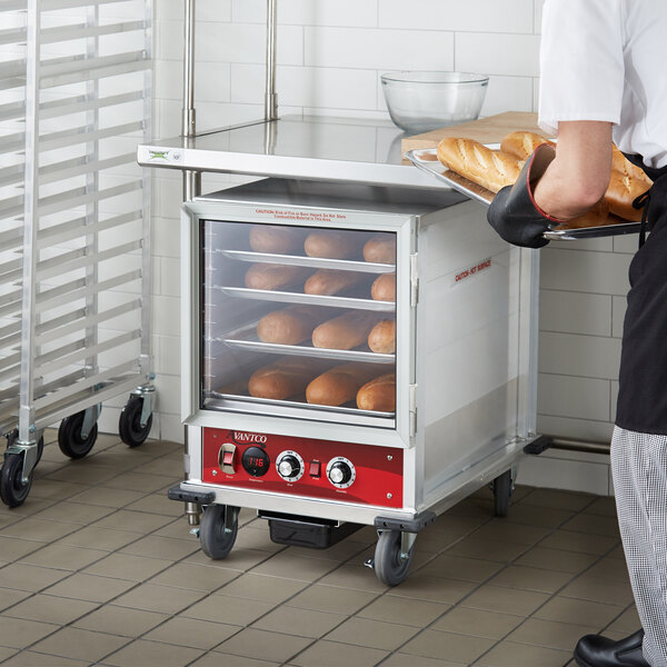 A man holding a tray of loaves of bread in an Avantco heated holding cabinet.