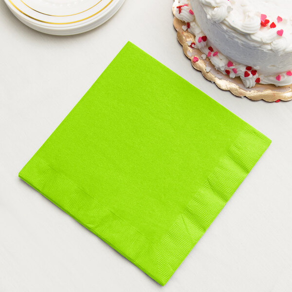 A Fresh Lime Green Creative Converting paper dinner napkin on a table with a white cake and red and pink sprinkles.