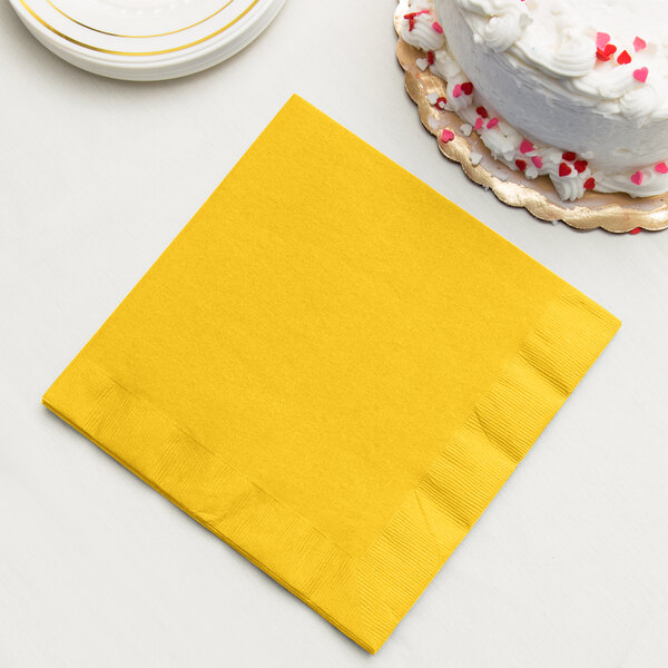 A yellow Creative Converting paper dinner napkin with a slice of cake on it.