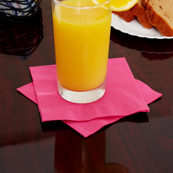 A glass of orange juice on a hot magenta pink Creative Converting beverage napkin.