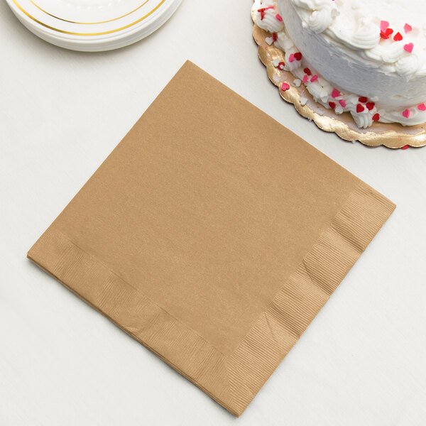 A Creative Converting Glittering Gold paper dinner napkin next to a plate of cake.