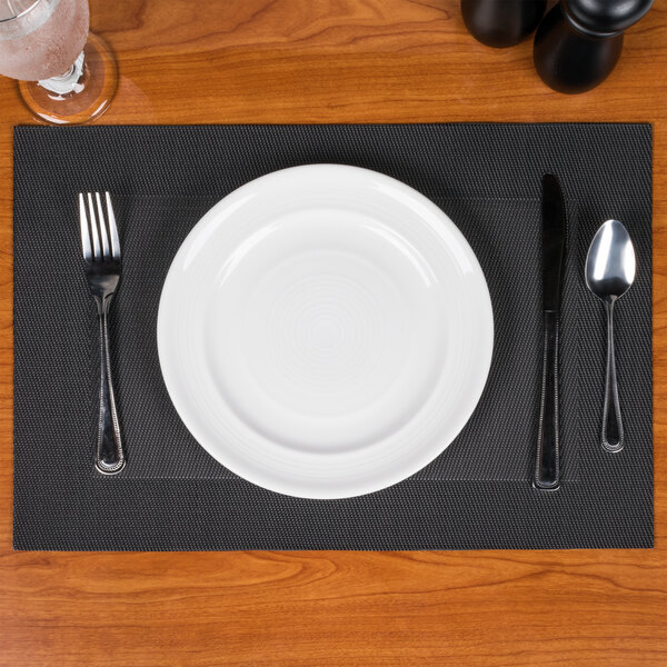 A Taos Charcoal PVC placemat with a plate, fork, and spoon on it.