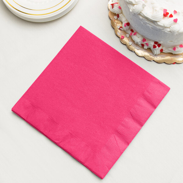 A hot magenta pink Creative Converting paper napkin next to a white cake.