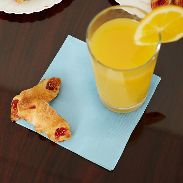 A glass of orange juice next to pastries with a Creative Converting pastel blue beverage napkin.