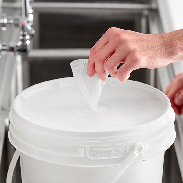 A hand putting a white bag of WipesPlus Center Pull Lemon Scent Alcohol Free Hand Sanitizing Wipes into a white bucket.