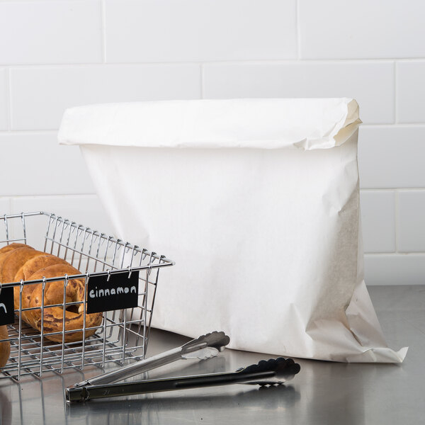 A Duro white merchandise bag in a basket on a counter with tongs and a basket of bread.
