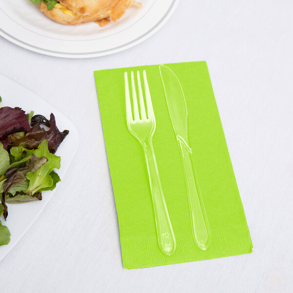 A fork and knife on a Fresh Lime Green Creative Converting guest towel next to a salad plate.
