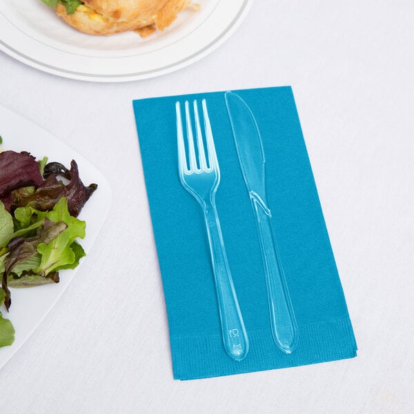 A turquoise blue guest towel with a fork and knife on it next to a plate of salad.