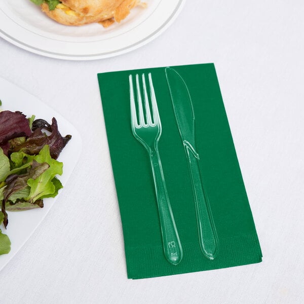 A green Creative Converting guest towel with a fork and knife on it next to a plate of salad.
