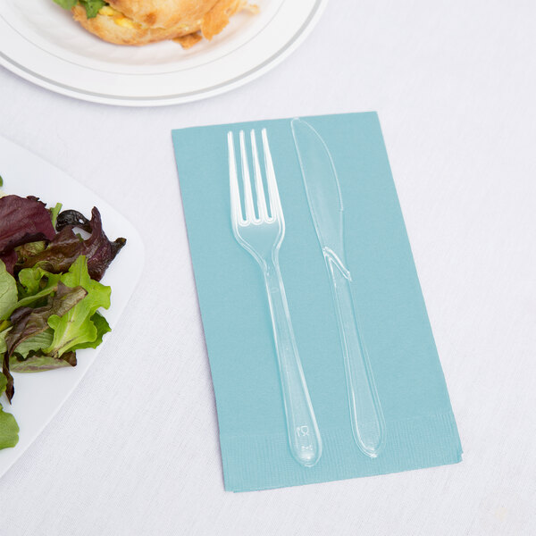 A Creative Converting Pastel Blue guest towel with a fork and knife on it next to a plate of salad.