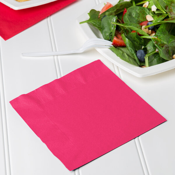 A hot magenta pink luncheon napkin with a fork on a plate of salad.