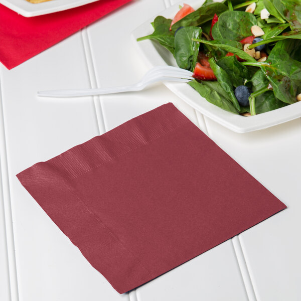A plate of salad with a burgundy luncheon napkin and a fork.