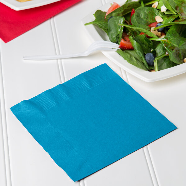 A turquoise blue Creative Converting luncheon napkin with a plate of salad and a fork.