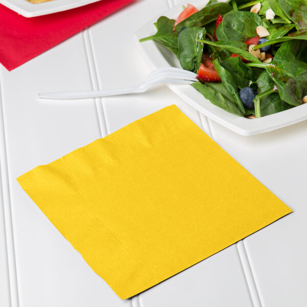 A yellow napkin next to a plate of salad.