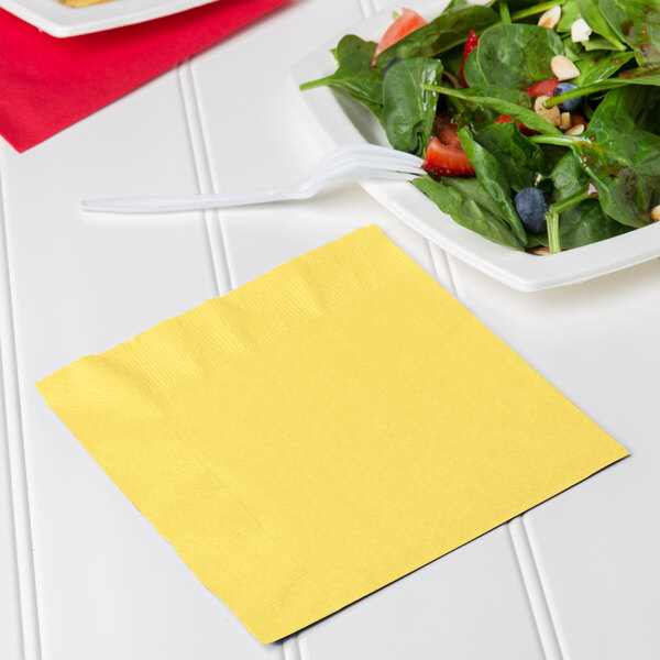A plate of salad next to a Creative Converting Mimosa Yellow luncheon napkin.