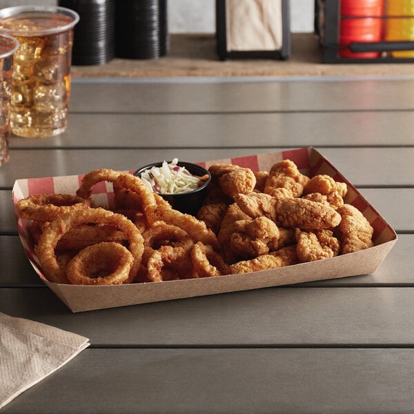 A box of fried food on a table with a red checkered paper food tray of fried chicken and fried onion rings.