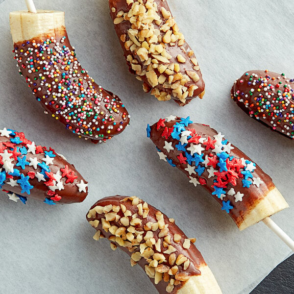 A group of Phillips chocolate covered bananas with sprinkles and nuts on a baking sheet.