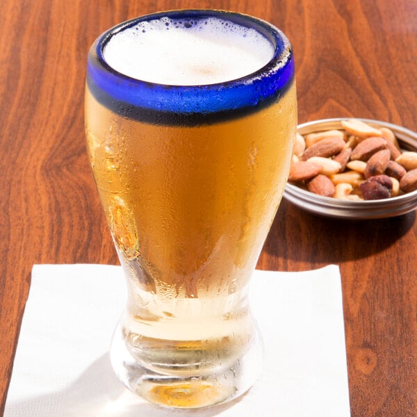 A Libbey pilsner glass with a bowl of nuts on a table.