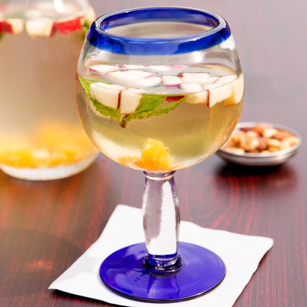 A Libbey Aruba cocktail glass filled with a blue drink and fruit slices and mint leaves.